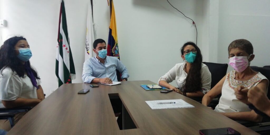 Reunión en una oficina institucional con banderas al fondo.
